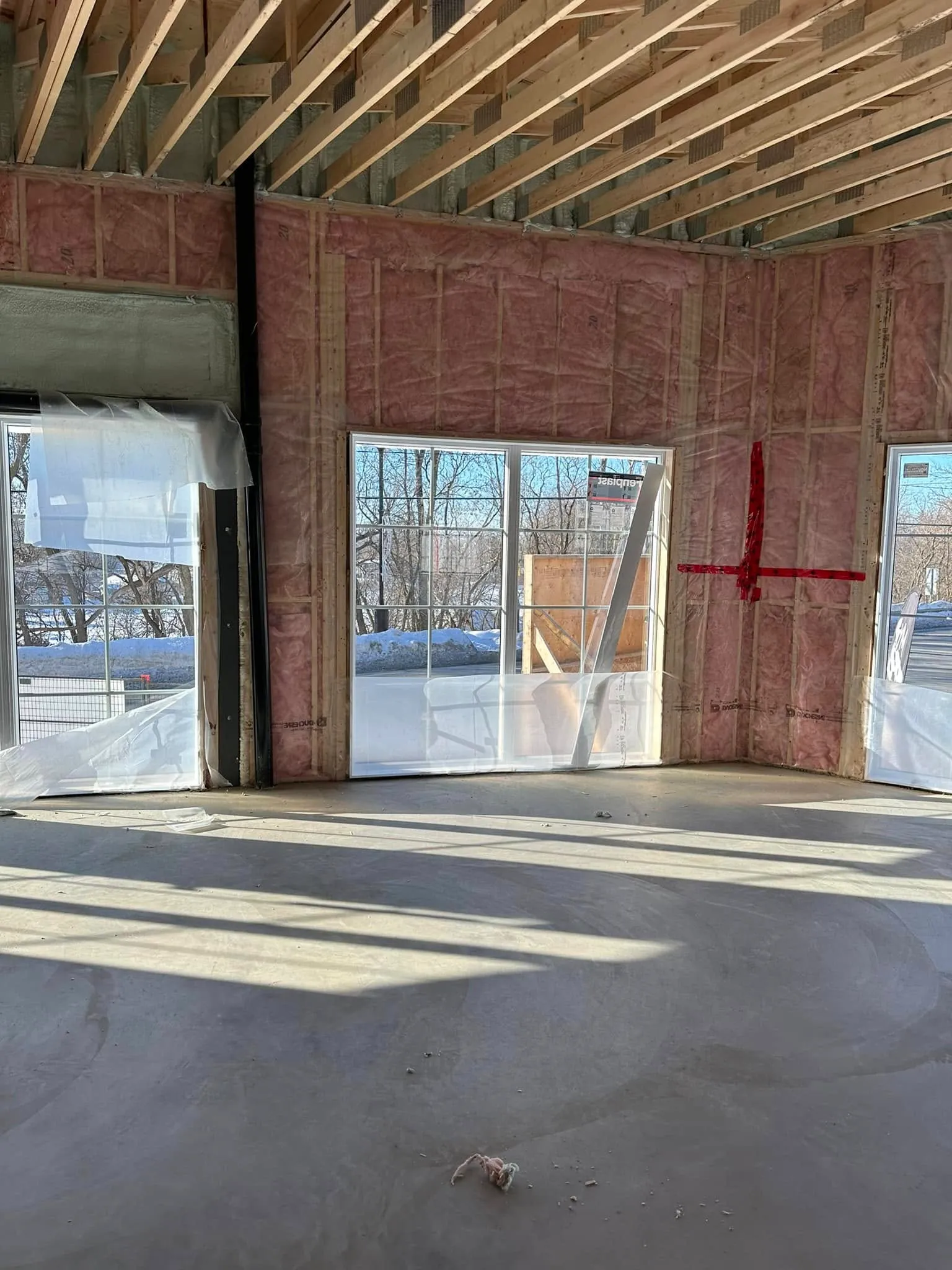 Intérieur en chantier : ossature de toit en bois, isolation et grandes fenêtres sur dalle de béton