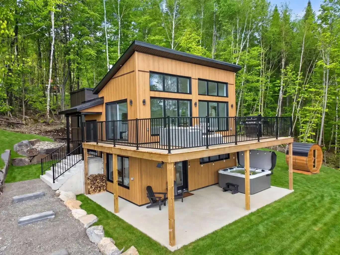 Façade du chalet en bardage de bois vertical avec terrasse sur poteaux et bain tourbillon