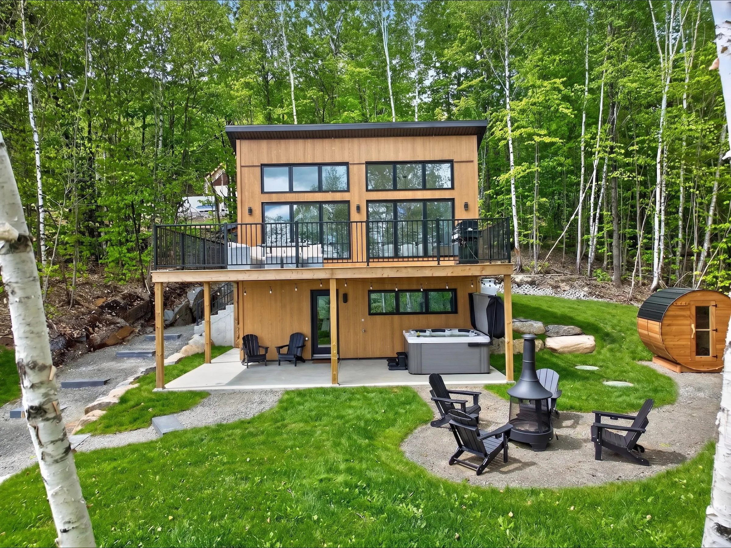 Le chalet vu du jardin, avec bain tourbillon sous la terrasse, foyer extérieur, chaises Adirondack et sauna en tonneau