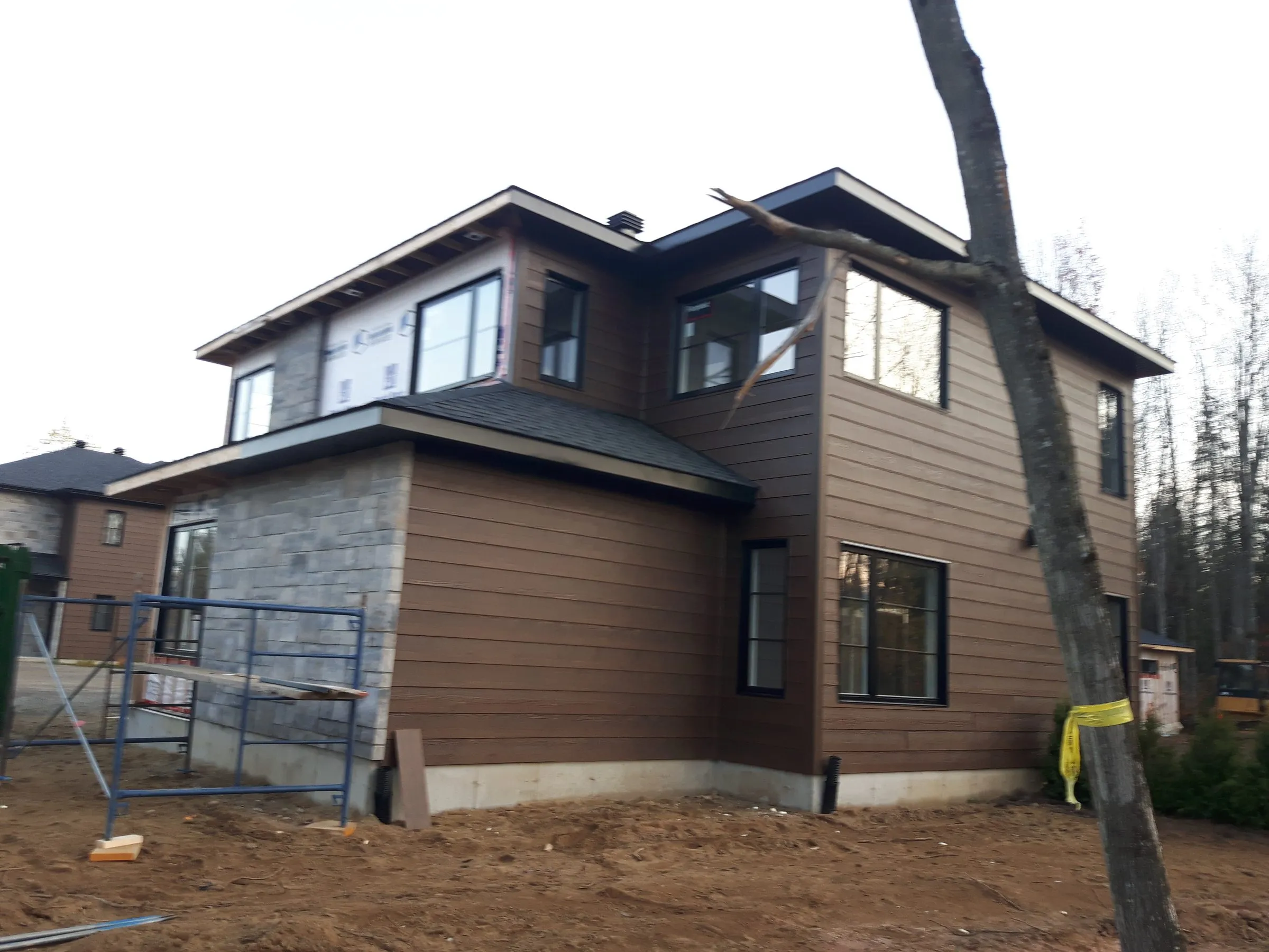 Angle du bâtiment avec parement bois brun posé et pierre au rez-de-chaussée, terrain encore en chantier