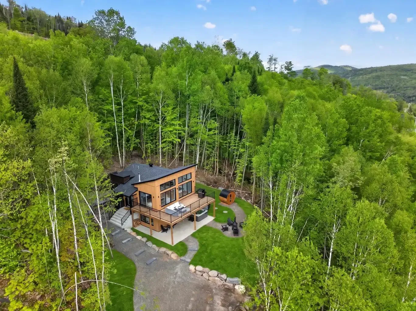 Vue aérienne du chalet en milieu forestier, avec son allée de gravier et sa cour aménagée