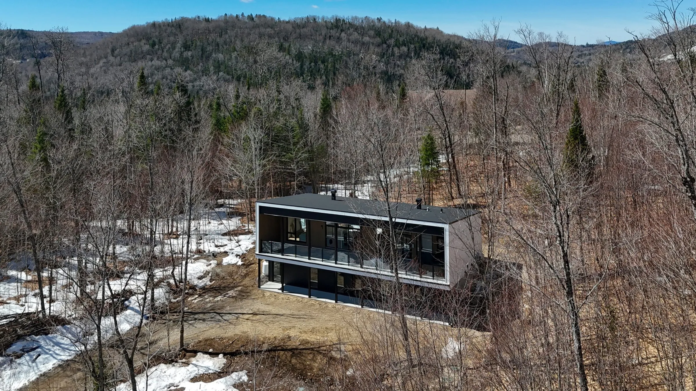 Vue aérienne du chalet à deux étages en bardage foncé, entouré de forêt en hiver