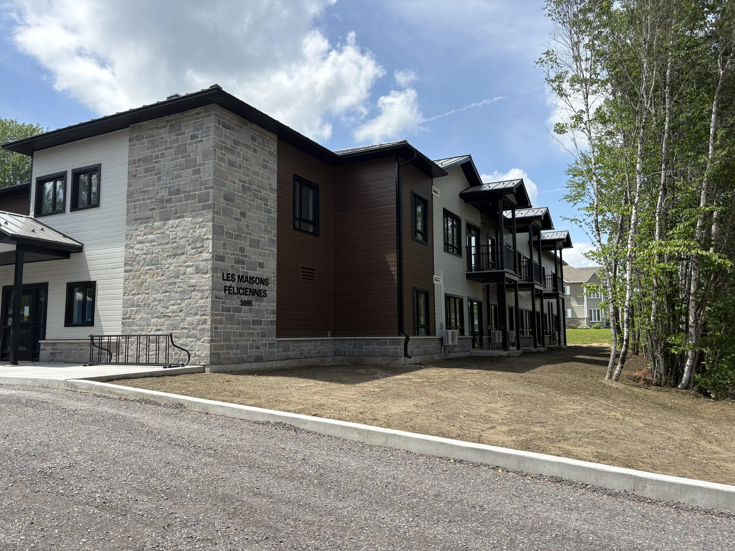 Immeuble en parement bois brun et blanc avec volume d'angle en pierre grise portant l'enseigne du projet