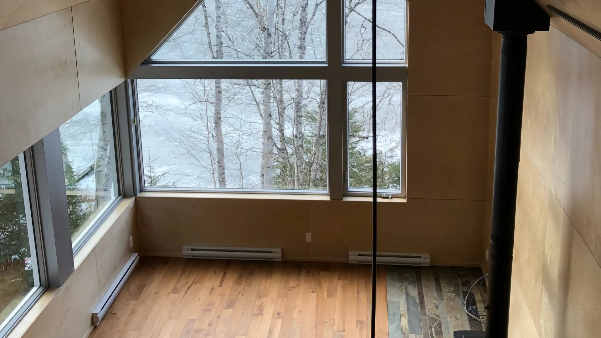 Fenêtres pleine hauteur sur la forêt enneigée, murs en bois clair et plancher de bois