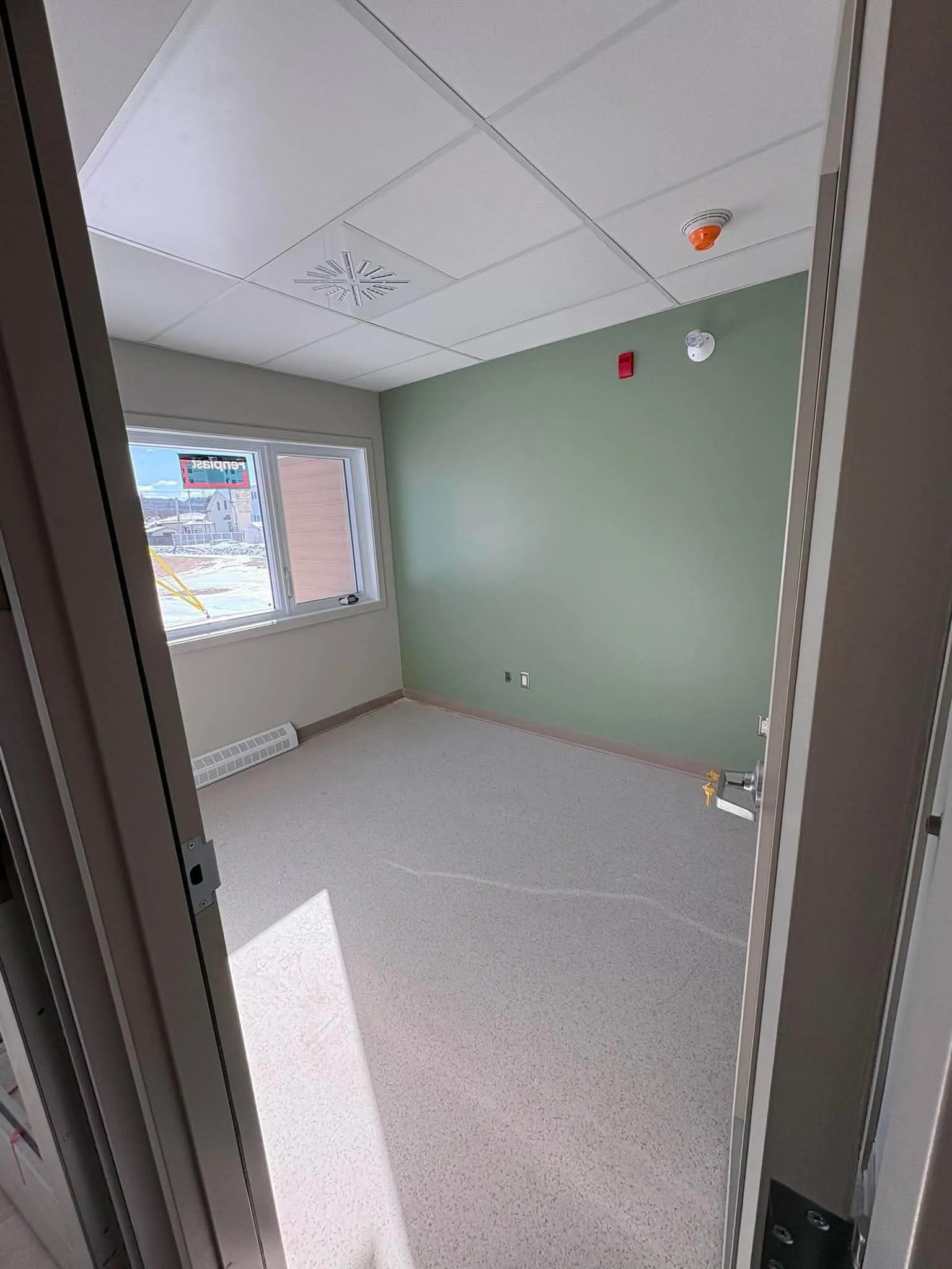 Local vide aux murs vert d'eau avec diffuseur de ventilation au plafond, détecteur de fumée et plinthe chauffante sous la fenêtre