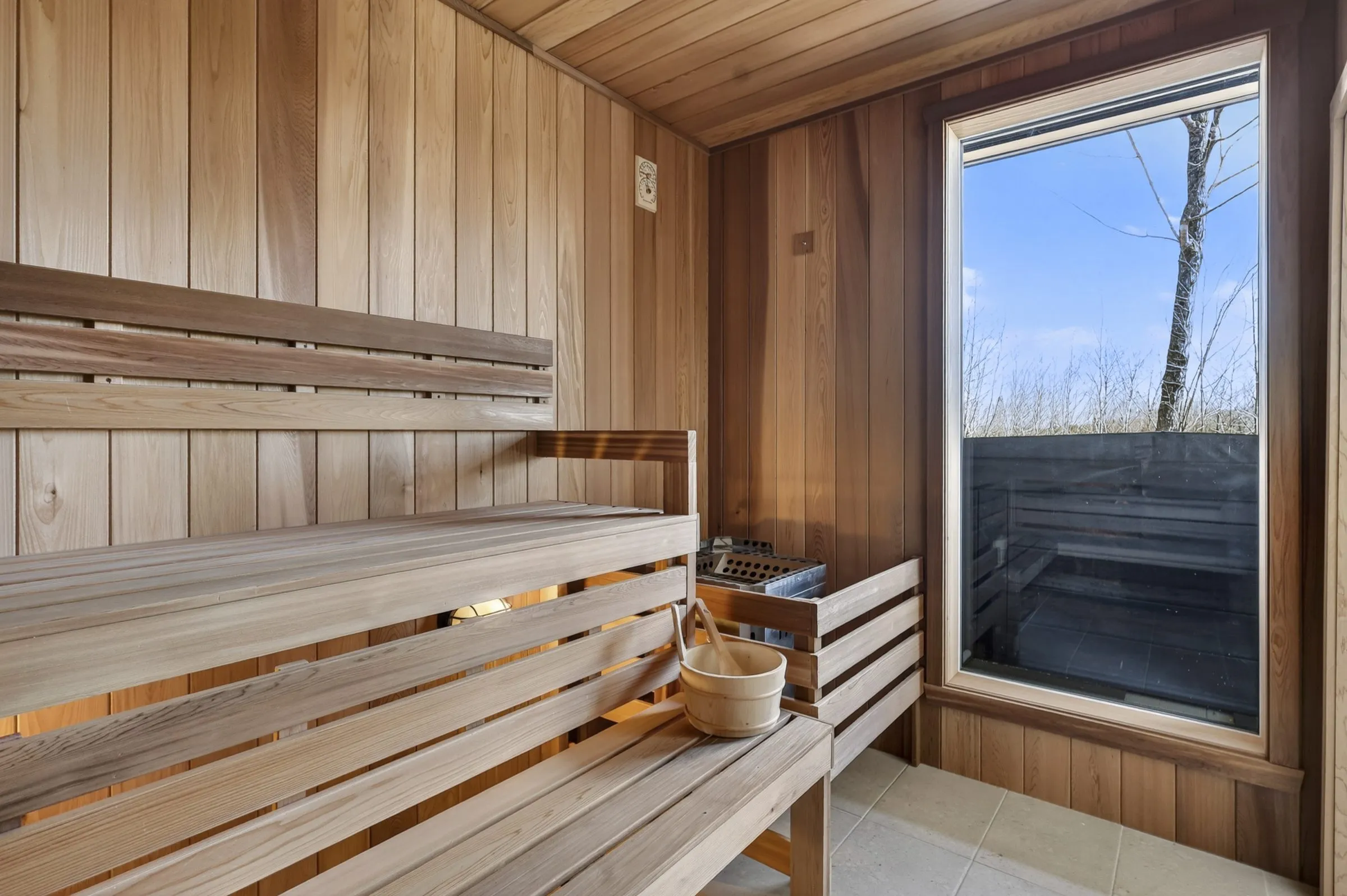 Intérieur du sauna en bois clair avec bancs à lattes et fenêtre sur la forêt