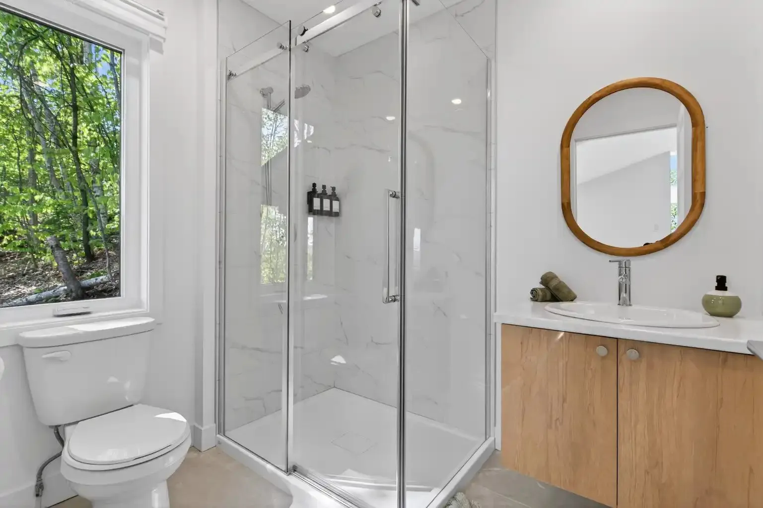 Salle de bain avec douche en verre, vanité de bois et miroir ovale